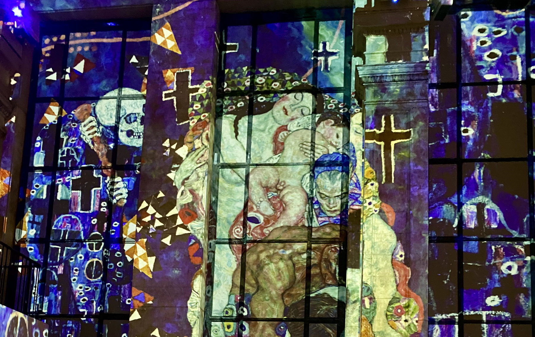 Colorful projected patterns across a gridded wall with faces and crosses